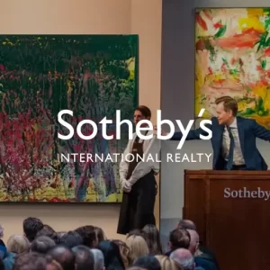 Art auction at Sotheby’s with a large abstract painting, auctioneer at podium, and audience, featuring Sotheby’s International Realty branding.